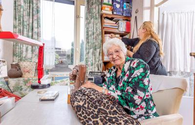 Mevrouw Staal zit achter de naaimachine terwijl Nancy schoonmaakt